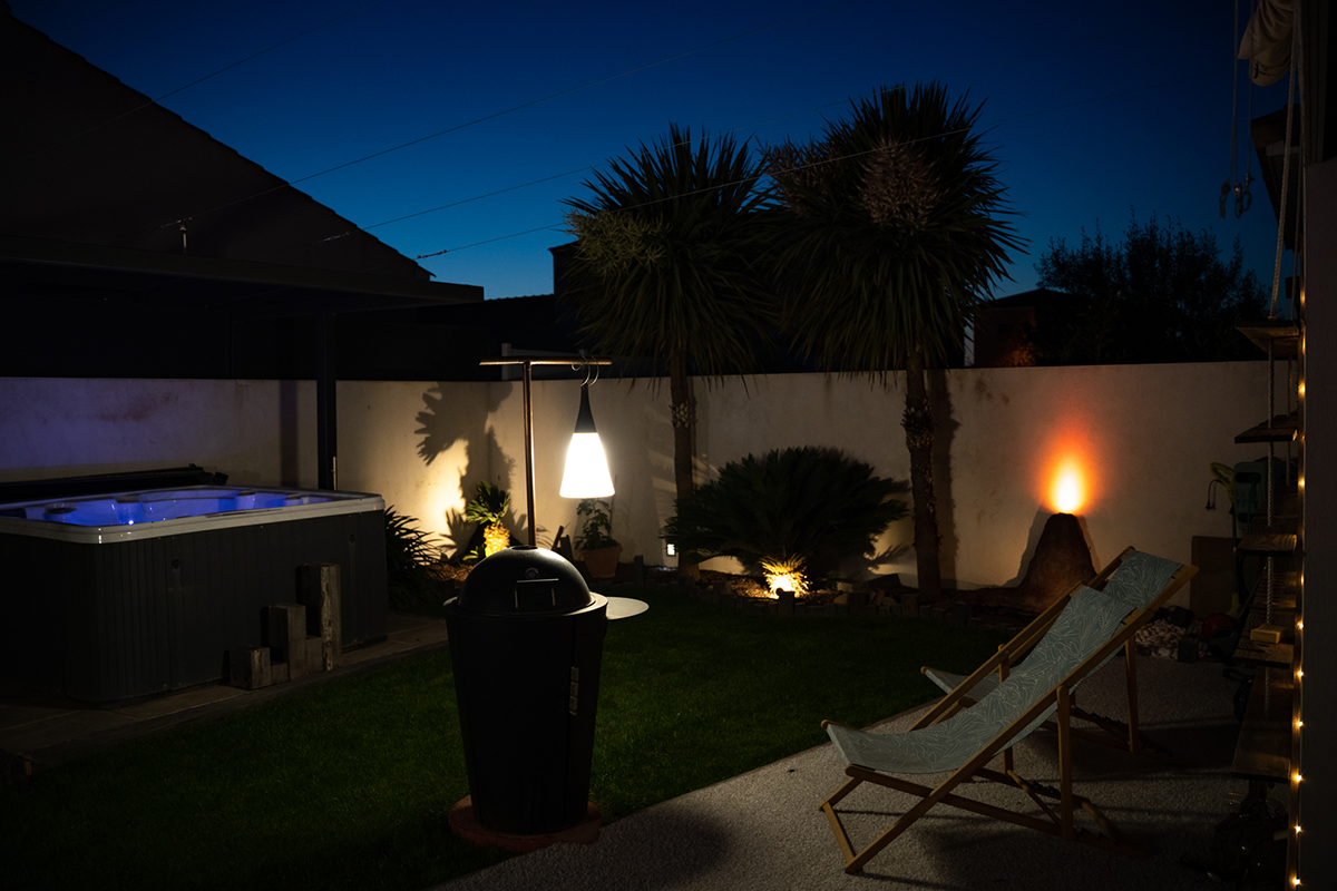 jardin de nuit éclairé avec chaises longues, plantes, jacuzzi ouvert avec éclairage allumé