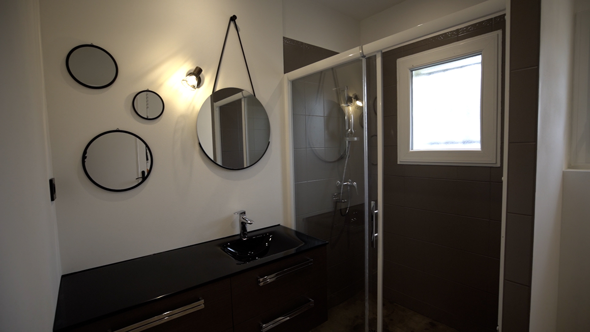 salle de bain éclairée par un spot mural au dessus d'un évier entre des miroirs ronds